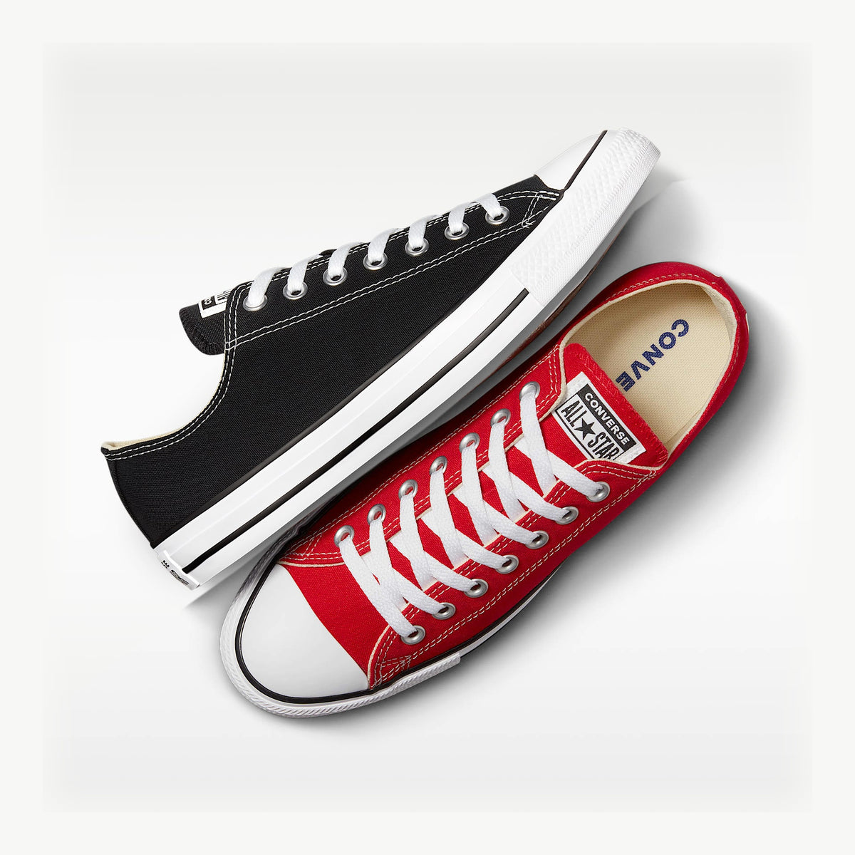Photo composite of one red and one black Converse Chuck Taylor All Star low top with the colours on the opposite feet